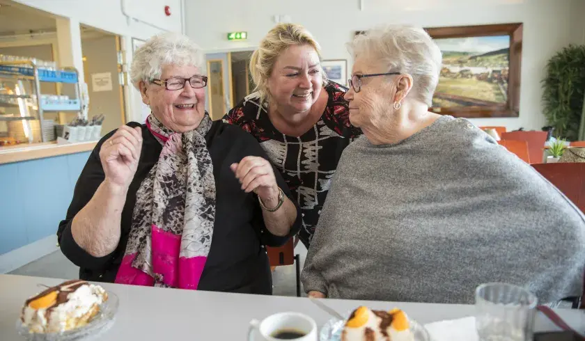 Tre damer koser seg sammen med kake og kaffe