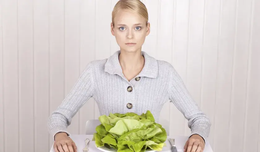 En jente som har spiseforstyrrelser sitter foran tallerken med grønne salatblader