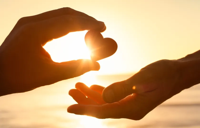 To hender holder et hjerte i solnedgangen